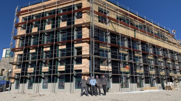 einger&uuml;steter 4-st&ouml;ckiger Holzbau, 5-k&ouml;pfiges Team steht davor